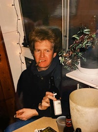 a man is smoking a cigarette and holding a bottle of wine