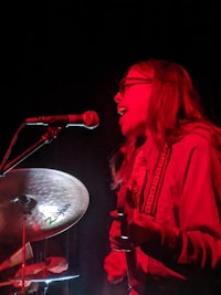 a woman singing into a microphone while playing drums